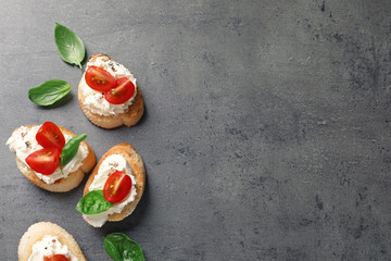 Pieces of baguette with tasty cream cheese and tomatoes on gray table, flat lay. Space for text