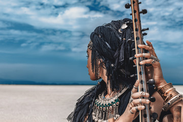 Wall Mural - Beautiful young stylish tribal woman in oriental costume playing sitar outdoors. Close up