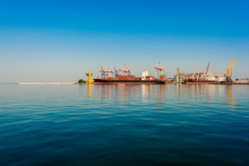 Container ship in the port on the horizon. Port crane loads a container on a ship. Cargo transportation by sea.