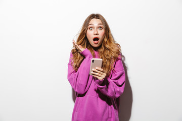 Canvas Print - Portrait of beautiful woman 20s wearing sweatshirt using mobile phone while standing, isolated over white background