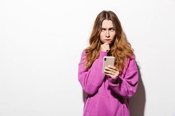 Canvas Print - Portrait of resentful woman 20s wearing sweatshirt holding mobile phone while standing, isolated over white background