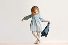 Full Length Portrait Of Cute Little Kid Girl In Stylish Jeans Clothes Looking At Camera And Smiling, Standing Against White Studio Wall. Kids Fashion Concept