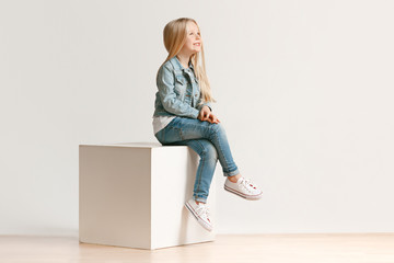 the portrait of cute little kid girl in stylish jeans clothes looking at camera and smiling, sitting