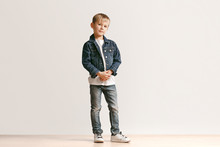 The Portrait Of Cute Little Kid Boy In Stylish Jeans Clothes Looking At Camera Against White Studio Wall. Kids Fashion Concept