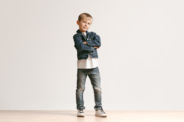 the portrait of cute little kid boy in stylish jeans clothes looking at camera against white studio 