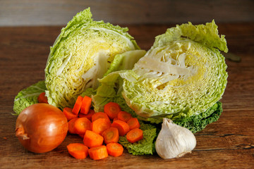 Wall Mural - Green savoy cabbage and other vegetables on vintage wooden table. With garlic, onion and carrot.