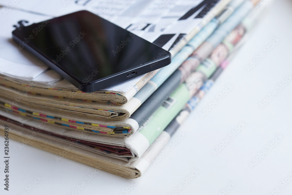 Newspaper and smartphone. Daily papers with news and black mobile phone with touch screen. Modern gadget and folded journal with articles. Electronic device on top of stacked pages, selective focus
