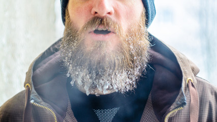 Wall Mural - Young man with a beard covered with icicles and frozen droplets on the street after exercise. Evaporation from the mouth in winter