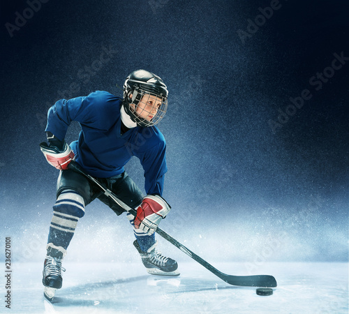 Obrazy Hokej  maly-chlopiec-grajacy-w-hokeja-na-arenie-hokeista-w-mundurze-z-wyposazeniem-na-niebieskim