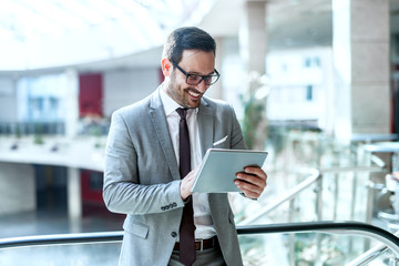 Smiling businessman using tablet for reading e-mail while standing near fence in business center.