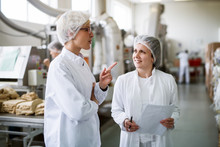 Two Female Workers Discussing While Standing In Food Factory.