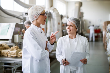 Two female workers discussing while standing in food factory.