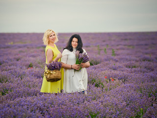 Two young girls with different hair color in white and yellow dresses, posing together in a lavender field.