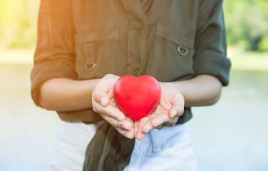 woman holding red heart in hands on outdoor or green natural background. people, age, family,insurance. love and health care concept