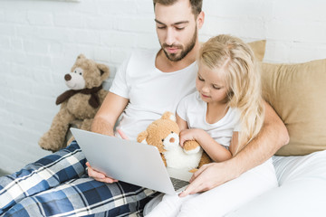 father and adorable little daughter using laptop together on bed