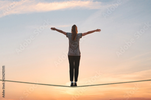 Fotografía A girl stands on the rope and raises her hands against the sunset