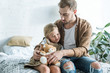 © LIGHTFIELD STUDIOS - father looking at cute little daughter sitting with teddy bear on bed