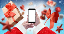 Santa's Hands Holding Black Phone With Isolated Screen On Blue Background Surrounded With Gift Box, Red Ribbon And Xmas Tree Ornaments. Mockup