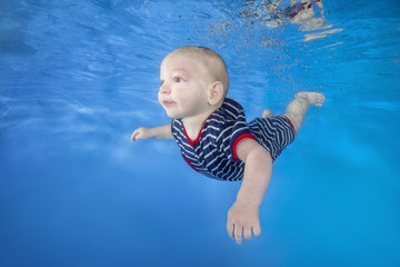 Little boy in a striped suit swim underwater on a blue water background.  Healthy family lifestyle and children water sports activity. Child development, disease prevention