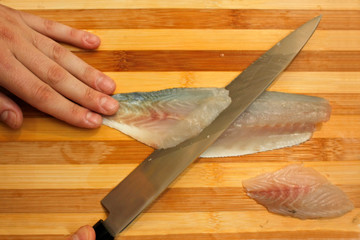 Chef's hand cutting  fish into thin slices with a knife.Fish fillet on a wooden cutting board.