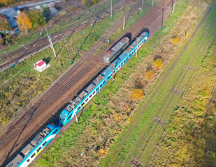 Aerial view on blue passenger train moving on rails in city area.