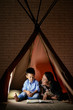 © DragonImages - Mother and son sitting in tent at home and reading a book