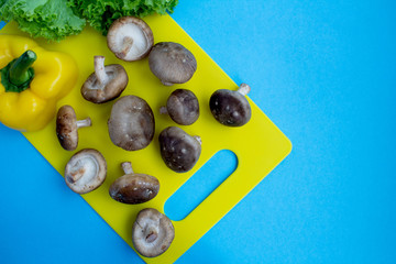 Wall Mural - Mushrooms shiitake and vegetables in the yellow cutting board on the blue background.Top view.Copy space.Healthy food ingredients.