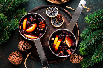 Canvas Print - hot mulled wine cooked in two saucepan with spices, orange and cranberries on the table with Christmas fir twigs on a dark background