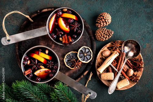 Fotografía hot mulled wine cooked in two saucepan with spices, orange and cranberries on th