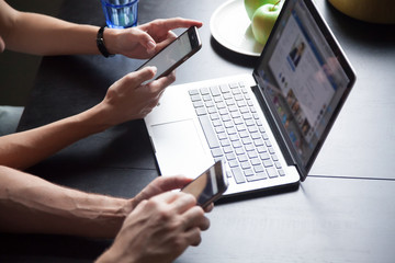 Wall Mural - Young couple using smartphones with laptop, texting, checking social networks at home, female and male hands holding phones, browsing websites concept, close up