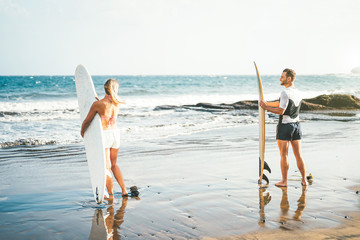 Wall Mural - Young couple of surfers standing on the beach with surfboards preparing to surf on high waves - Sporty people having fun during a surfing day