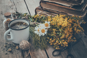 Wall Mural - Enameled mug of healthy tea, bunches of medicinal herbs and stack of old books. Herbal medicine.
