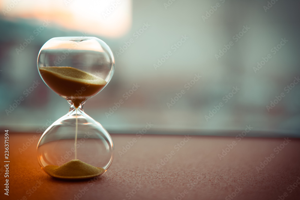 Sand running through the bulbs of an hourglass measuring the passing time in a countdown to a deadline, on a blur background with copy space - obrazy, fototapety, plakaty 