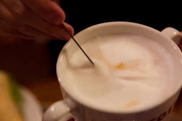 A man's hand mixing with spoon of latte