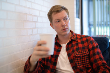 Young Handsome Hipster Man Thinking While Holding Coffee