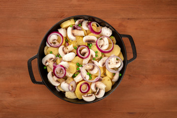 Wall Mural - A photo of a braiser with raw vegetables, potato, onion, green peas, and mushrooms, shot from the top on a dark rustic background, a vegan dinner