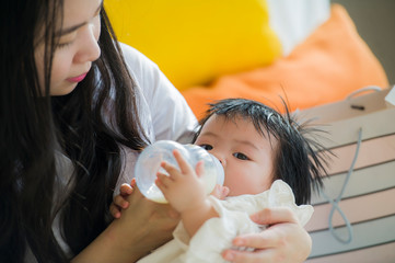 lifestyle candid portrait of young happy and sweet Asian Korean woman feeding her beautiful baby girl with formula bottle at holidays resort as mother nursing daughter