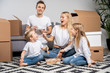 © snedorez - Photo of happy couple with children eating rice with shrimps sitting on floor among cardboard boxes