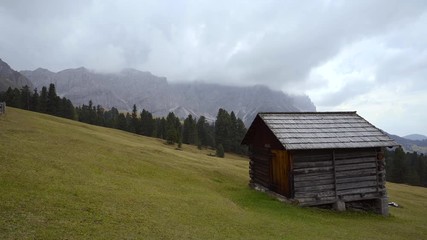 Wall Mural - Wooden sheds on a grassy meadow on the edge of the forest with mountain rising in the background, Italian Dolomites.