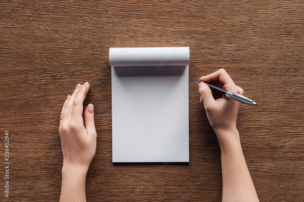 cropped view of person holding pen over blank notebook on wooden background - obrazy, fototapety, plakaty 
