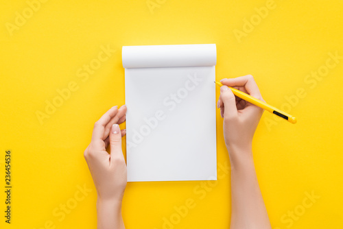 Fotomural partial view person holding pen over blank notebook on yellow background