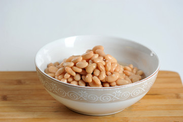 canned white beans in a deep bowl. wooden surface white background. close-up.