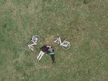 High Angle View Of Couple With Bicycles Lying On Grassy Field At Park