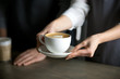 © fizkes - Close up of barista holding aromatic cappuccino, serving it to coffeeshop visitor, waitress giving cup of fresh brewed coffee with milk foam to cafe guest, bringing latte drink to coffeehouse table