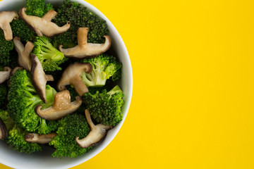 Wall Mural - Vegetarian salad with mushrooms shiitake and broccoli in the white bowl on the yellow background.Top view.Copy space.Healthy food ingredients.