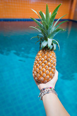 Wall Mural - Fresh yellow pineapple tropic fruit summer in woman hands carrying near pool