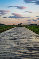 Wall Mural - waves in a dutch canal with a beautiful perspective. a distant windmill stands at the end of the can