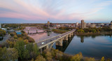 Fototapeta Niebo - Aerial panoramic view of a bridge going over Saskatchewan River during a vibrant sunrise in the Fall Season. Taken in Saskatoon, SK, Canada.