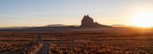Striking Panoramic Landscape View Of A Dirt Road In The Dry Desert With A Mountain Peak In The Background During A Vibrant Sunset. Taken At Shiprock, New Mexico, United States.