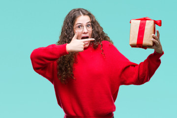 Sticker - Young brunette girl holding a gift over isolated background very happy pointing with hand and finger